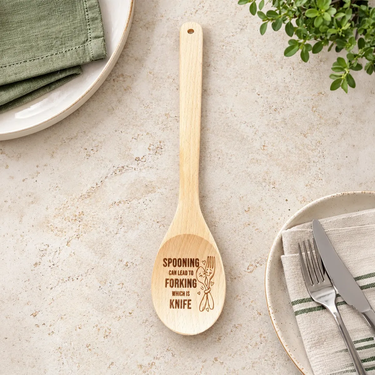 Spooning Can Lead to Forking Which Is Knife engraved wooden spoon, on a dining tabletop with plates and cutlery